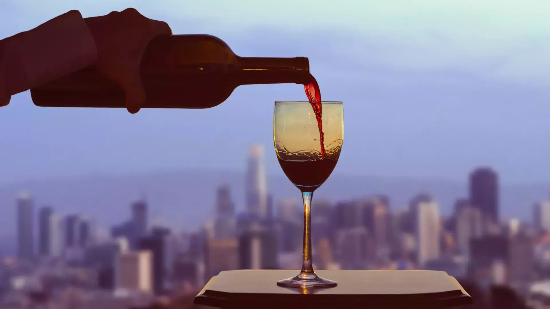 A glass of red wine being poured, with the San Francisco skyline visible out the window.