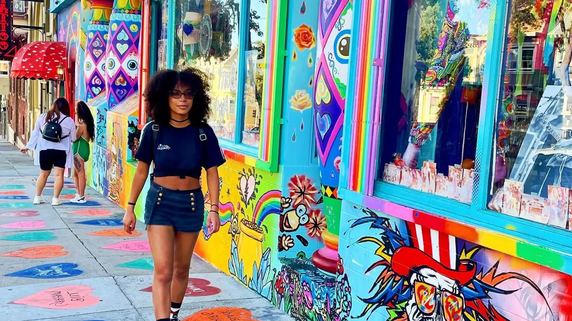 Woman walking down Haight Street with a colorful mural in the background.