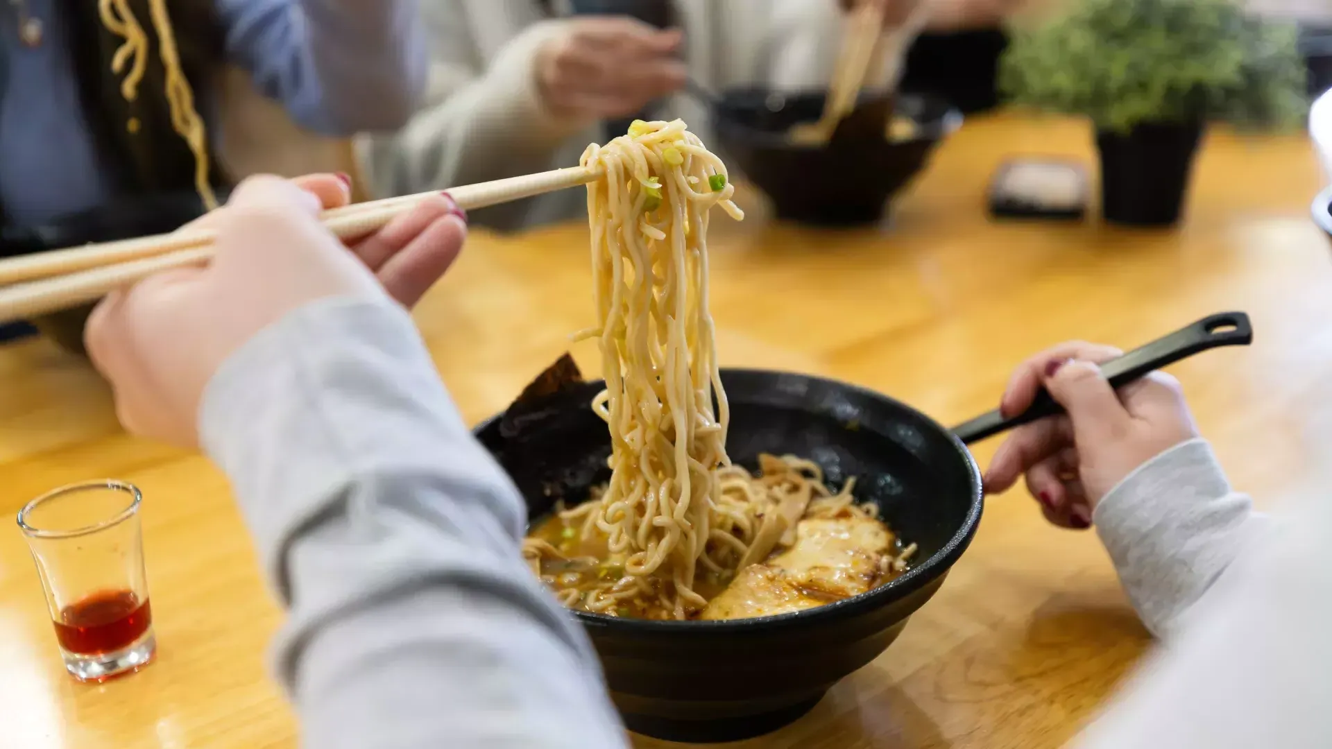 Person lifting ramen noodles out of a bowl with chopsticks