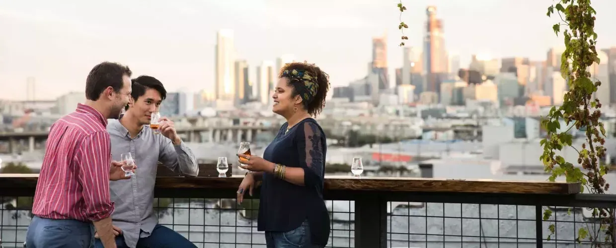 Three people gather around an outdoor table on the roof deck of Anchor Distilling in 贝博体彩app，加利福尼亚.