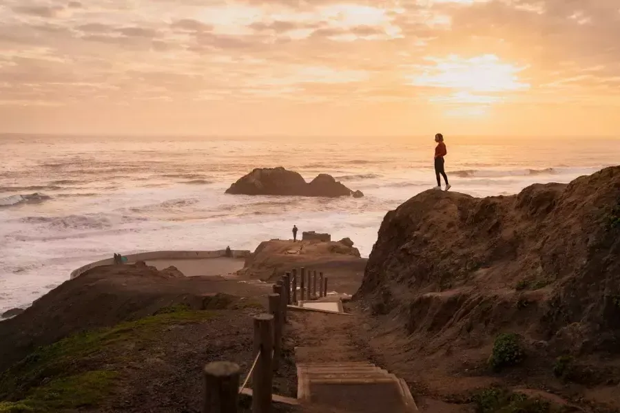 Due persone stanno sulle rocce che si affacciano sull'oceano ai Sutro Baths di San Francisco.