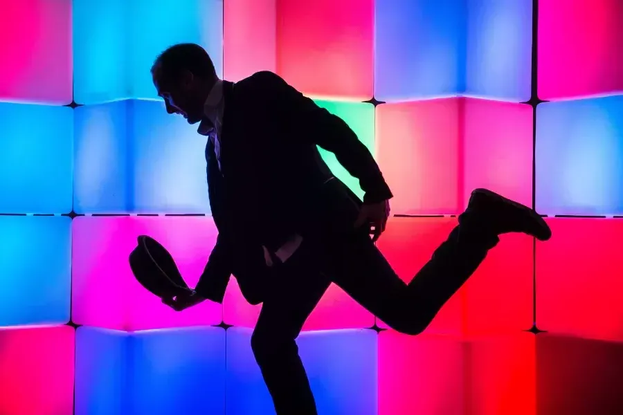 man in front of glowing boxes, posing and lowering hat in a bow position