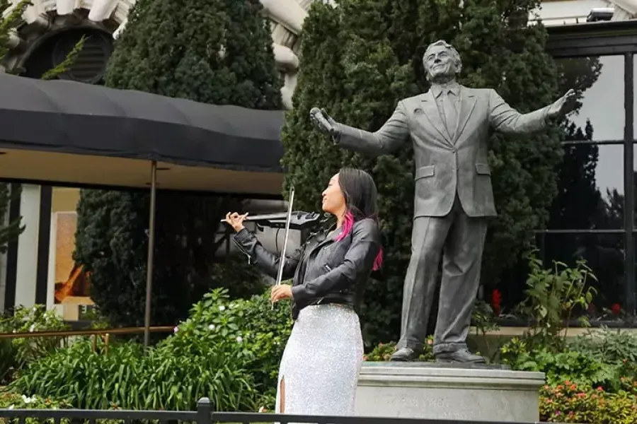 A woman plays the violin in front of the Tony Bennett statue at the Fairmont酒店.