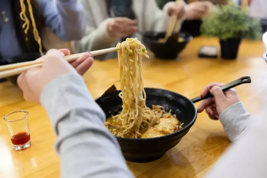 Person lifting ramen noodles out of a bowl with chopsticks