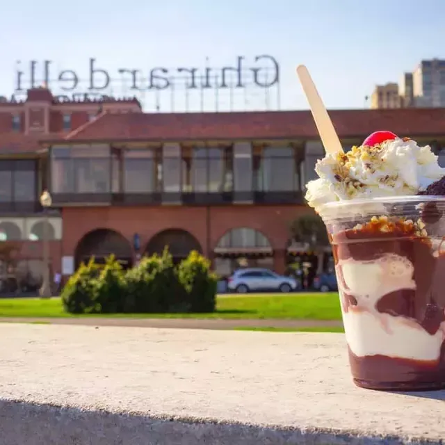 Un helado de chocolate se encuentra en primer plano con la plaza Ghirardelli al fondo.