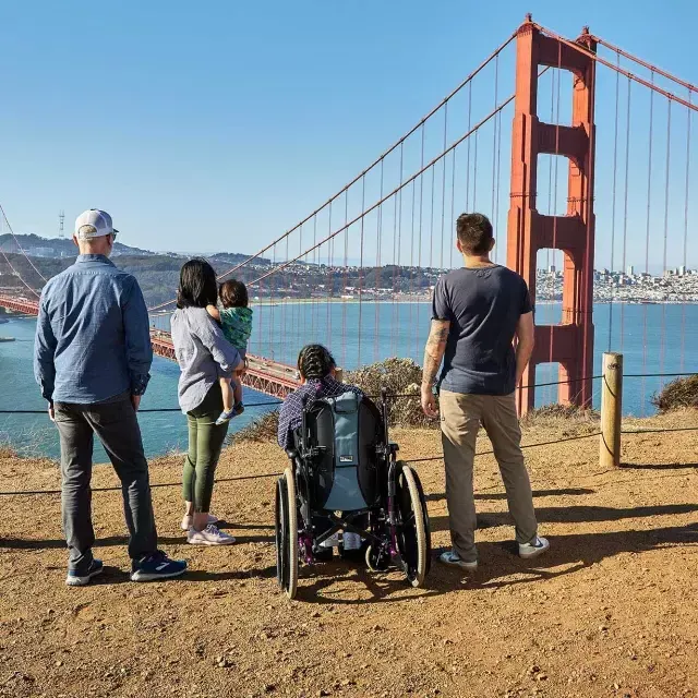 Un grupo de personas, 包括一名轮椅使用者, se ve desde atrás mientras miran el puente Golden Gate desde Marin Headlands.