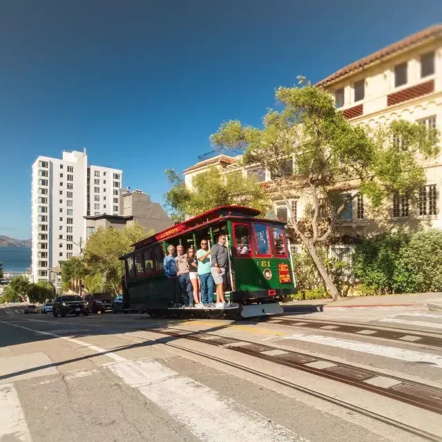 Teleférico Powell e Hyde subindo a rua com pessoas sorridentes dentro de um dia ensolarado.